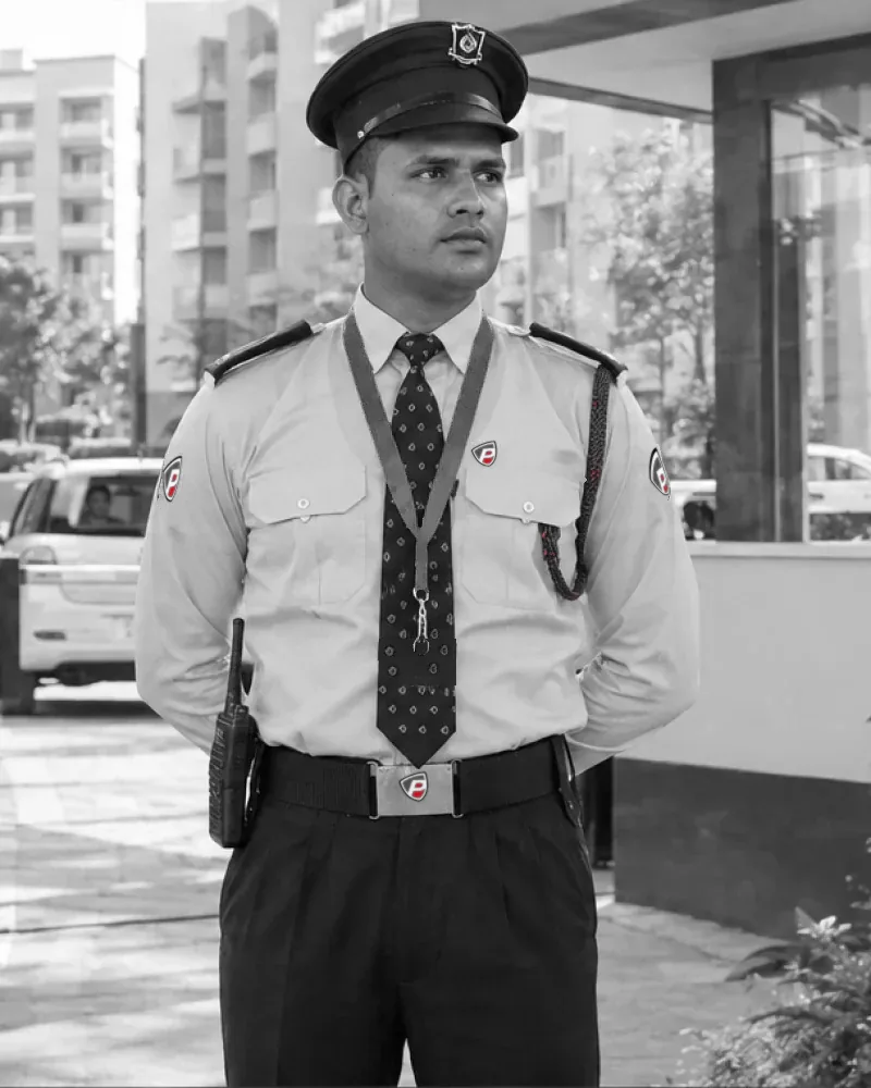 Security officer on gate duty at a residential society, in light blue uniform and cap, apartment blocks behind